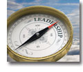 Photo of large compass with needle pointing to the word LEADERSHIP on sky background